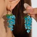 Close-up of blue crystal grape earrings with green leaf detail worn by a model - Blue