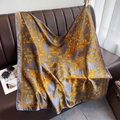 Baroque print silk square scarf in grey and gold draped over a brown leather couch - 90x90cm / Grey Gold (Yellow)