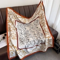 Silk-feel floral square scarf in white and orange draped over a leather sofa - White