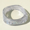 Macro shot of wide resin bangle with colorful glitter and sparkling light reflections - White