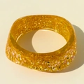 Gros plan d'un bracelet en résine ambrée translucide avec feuilles d'or et paillettes - Orange