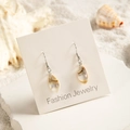 Detailed view of beach-style shell leaf earrings on a fashion display card with sand background - Brown White Leaf Shape Style (29368-8)