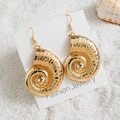 Dettaglio di orecchini a conchiglia dorata con texture a spirale su sfondo di sabbia - Stile Nautilus d'Oro (29422-4)