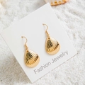 Détail de boucles d'oreilles bohèmes en coquillage doré avec texture nacre sur sable - Style Coquillage à Rayures Texturées (29421-1)