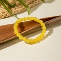 Dettaglio di perline acriliche gialle traslucide su corteccia con foglie verdi fresche - Giallo