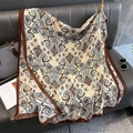 Detail of soft paisley print scarf draped on leather sofa with luxury travel accessories - Beige