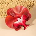Macro detail of red orchid flower hair clip on woven straw mat for beach vacation style - Red