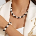 Dettaglio del set collana e bracciale gotico con teschi indossato su un abito bianco - Set Collana Bracciale Scheletro Nero Bianco (30440-NB-bw-set)
