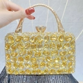 Close-up of golden luxury evening bag with sparkling crystals and bamboo-style handle - Gold