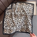 Dettaglio di sciarpa leopardata in finta seta con bordi neri su pelle marrone - Leopardo Cachi Riso