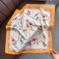 Dettaglio di un foulard di seta satinata a fiori con bordo arancione e catena dorata - Arancione