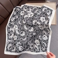 Detailed view of elegant black and white floral silk scarf on a premium leather surface - Black