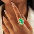 Opvallende gouden ring met grote iriserende groene steen gedragen door model - Smaragdgroen (Kunstmatige Parel)