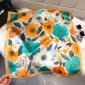 Elegant floral silk square scarf with orange lily print styled on a plush white surface - Orange Green (Modern Floral)