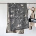 Detail view of dark grey winter scarf with maple leaf print and fringe hanging on a rack - Gray
