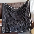 Close-up of elegant black silk scarf with white polka dots on a brown leather surface - Black