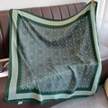 Detailed close-up of green silk scarf with floral monogram pattern on leather sofa - 90*90cm / Green