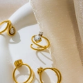 Detailopname van gouden spiraalringen met ronde zirkonia op wit keramiek plateau - US 6 / Grote en Kleine Ronde Zirconia