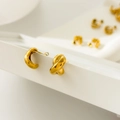 Detailed macro view of 18K gold plated twisted croissant earrings on a white stand - Curved Cross
