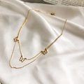 Detalle de collar de doble capa dorado con colgantes de mariposa sobre seda blanca - Dorado