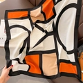 Detail eines Seidenschals mit geometrischem Kontrast auf braunem Ledersofa-Hintergrund - Beige-Orange