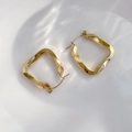 Detailed view of gold twisted square hoop earrings on a rippling water background - Twisted Style
