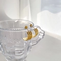 Close-up of triple-layered golden C-shaped hoop earrings on a textured glass rim - Triple Layer Style