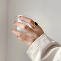 Dettaglio di un anello a sigillo dorato con onice nero tenuto da una mano con un vetro - US 6 / Rettangolare