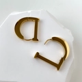 Detailed view of polished gold D-shaped earrings on a white minimalist stone base - D Style / Gold