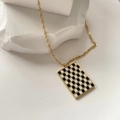 Close-up of golden rope chain with black and white checkered rectangle pendant on stone - Rectangle