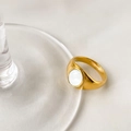Vue détaillée d'une bague chevalière dorée avec nacre blanche sur un bord en verre - Coquillage Blanc