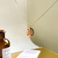 Macro shot of gold-plated pendant necklace with pink enamel shell and floral design - Clam