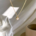 Detail of a gold-tone one-carat zircon pendant necklace with a round-cut stone on white silk - Clear White