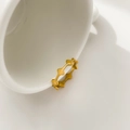 Detail of a gold geometric cross star ring hanging on a white ceramic cup edge - Geometric Rhombus Starburst Style