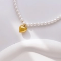 Detail of white pearl necklace with a golden heart pendant on white stone props - Round Pearl Large Heart