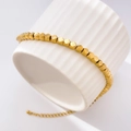 Close-up of gold fish scale chain bracelet with geometric beads on ceramic base - Geometric Square Bead Style