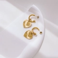 Detail goldener Herzohrringe mit Sonnenstrahl-Textur auf minimalistischem Hintergrund - Sonnenschliff-Muster-Stil / Goldener strukturierter Herz-Reifen