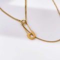 Detail van een minimalistische gouden veiligheidsspeld hanger aan een fijne ketting - Speld Stijl