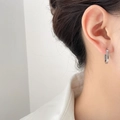 Detailed view of polished silver U-shaped huggie earrings worn on a model's ear - U-Shape Steel Color / Steel