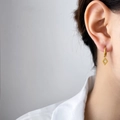 Orecchini a cerchio dorati con pendente a rombo inciso a stella indossati da una modella - Piastra a Rombo Piccola Zirconia