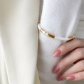 Detail van een witte emaille en gouden kralen armband over een witte gebreide mouw - Wit Emaille Open Stijl