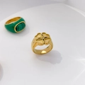 Detail of a gold signet ring with floral motif and green enamel clover ring on a white base - Four-leaf Clover
