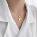 Primer plano del collar dorado con colgante de corazón irregular en una camisa blanca - Corazón Puntiagudo