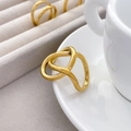Close-up of twisted 18K gold plated stainless steel ring on a white ceramic cup - US 6 / Cross Knot