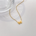 Détail du collier papillon doré à deux couches avec texture coquillage sur fond blanc - Papillon Poli