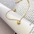 Detail of a polished gold heart pendant on a delicate chain over book pages - Heart Pendant Fine Chain Style