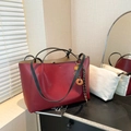 Minimalistische weinrote Tote Bag mit schwarzen Henkeln und Innentasche auf Holztisch - Rot mit Anhänger
