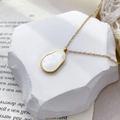 Gros plan du pendentif en nacre ovale sur un collier délicat en titane plaqué or 18 carats - Coquille en forme de melon