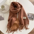 Detail of caramel and brown cashmere-like scarf with fringe and brand label on table - Dusty Pink