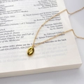 Detail of 18K gold-plated oval pendant with star engraving and zircon on vintage book page - Oval Starburst